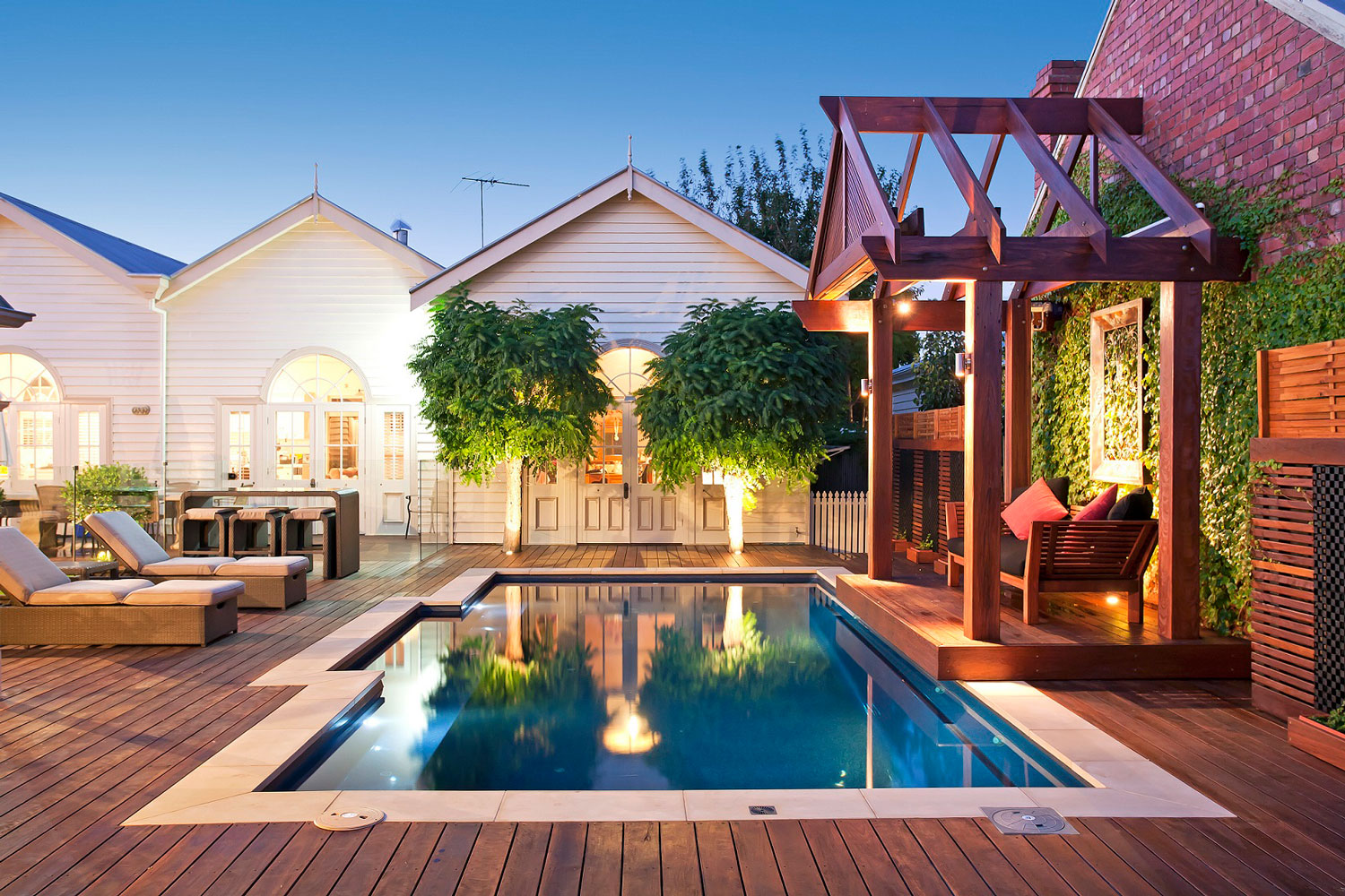 Freeform fiberglass pool glowing at dusk beside a timber pergola